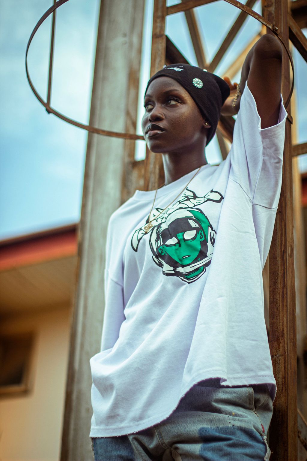 A young creative in a branded white tee and headwrap, arm raised against an open sky